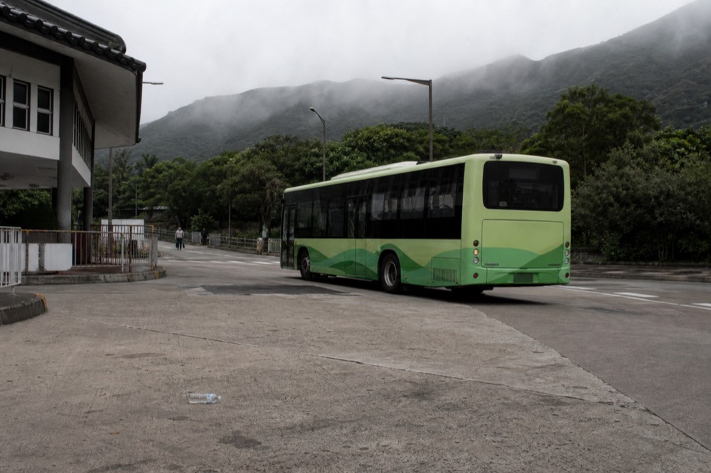 A green mountain bus on a winding hillside road above the sea, no text, no logos, no people