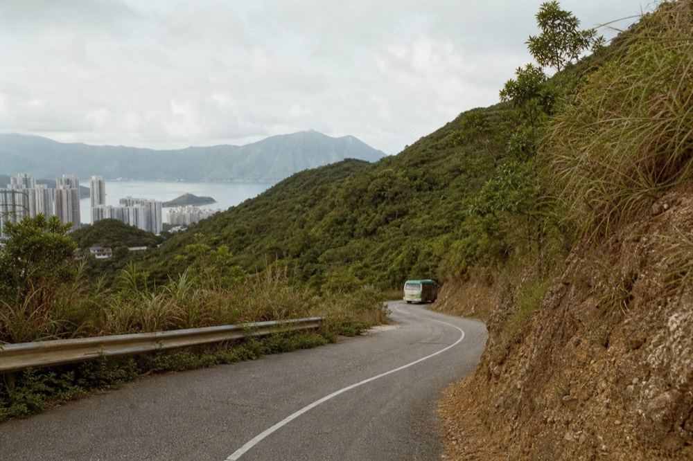 A narrow Lantau mountain road curving through green hills above Tai O, no text, no logos, no people