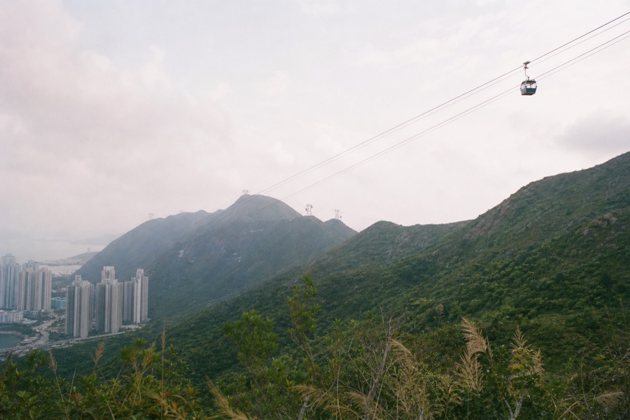 Cable car cabins gliding above Lantau's green hills toward the Ngong Ping plateau, no text, no logos, no people.