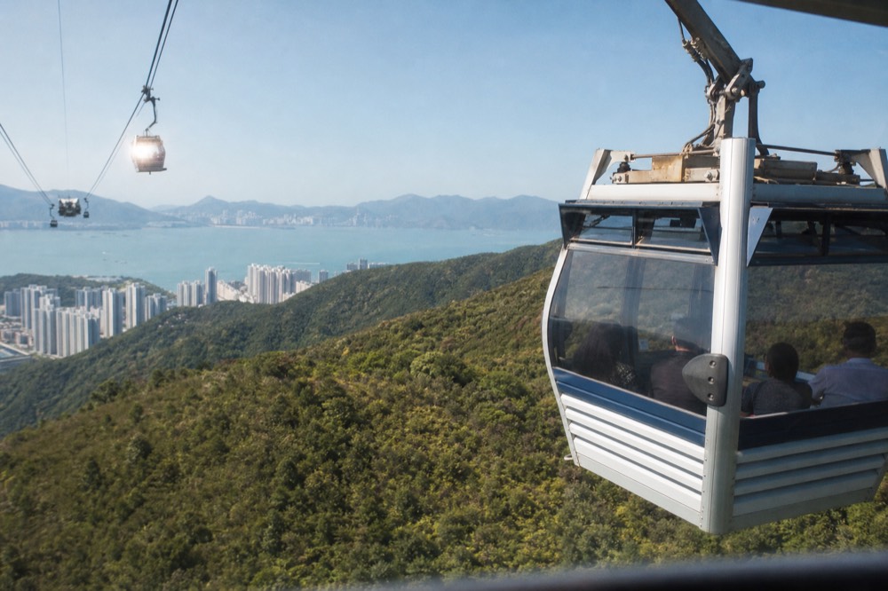 A cable car cabin travelling above green Lantau hillsides toward a high plateau, no text, no logos, no people