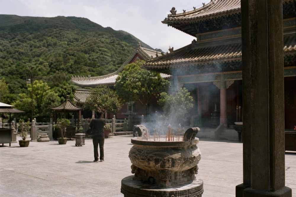 Rooflines of Po Lin Monastery with incense and courtyard, hills behind, no text, no logos, no people