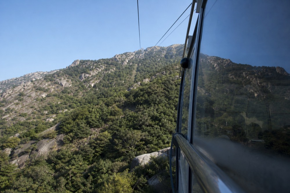 A modern cable car cabin with extensive glass panels travelling above a wooded ridge, no text, no logos, no people.
