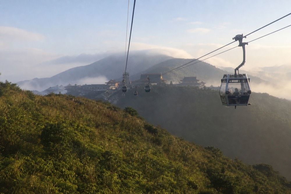Cable car cabins gliding over the Lantau hillside toward the Ngong Ping plateau, no text, no logos, no people