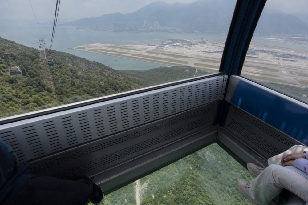 A glass-floor cable car cabin high above green slopes near the airport, no text, no logos, no people