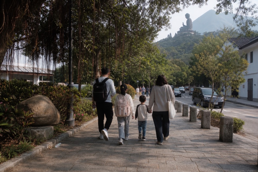 A family walking the path between Ngong Ping Village and the Big Buddha steps, no text, no logos, no people.