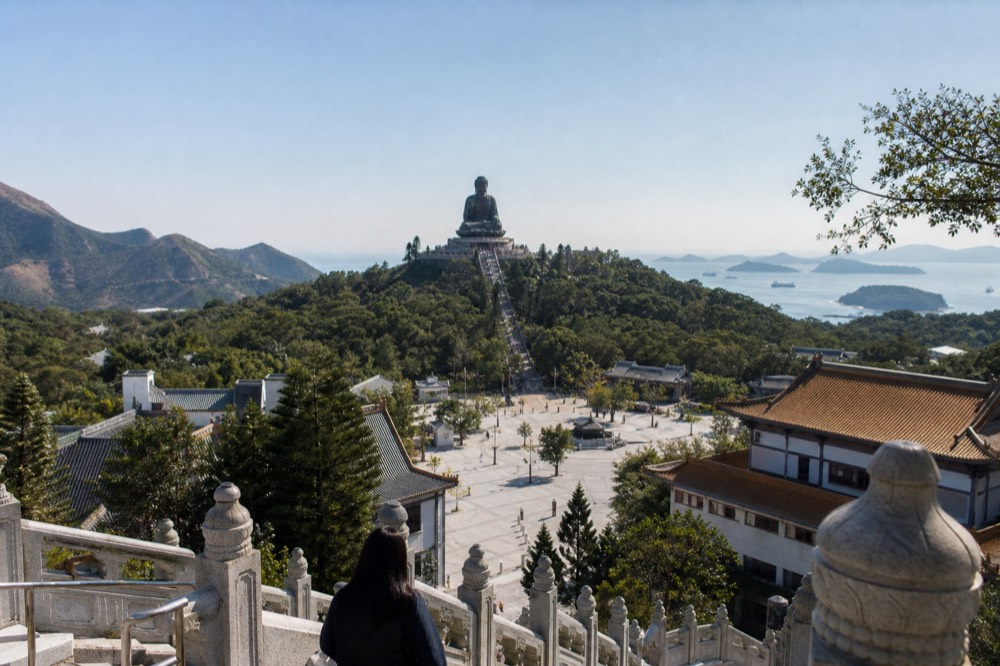 Clear autumn sky over the Lantau plateau with the monastery rooftops below the Buddha, no text, no logos, no people