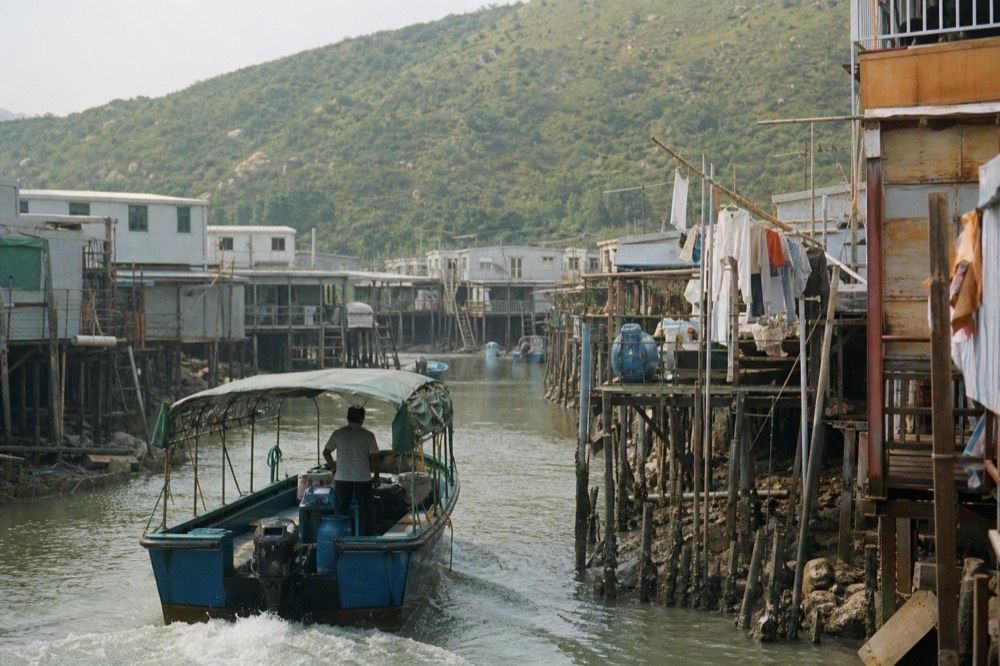 A small boat passing stilt houses along the water channel in Tai O fishing village, no text, no logos, no people