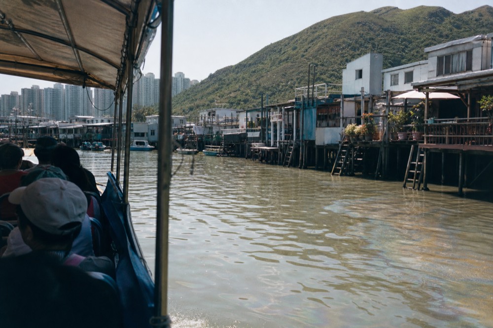 A tour boat cruising past stilt houses on the water channel at Tai O fishing village, no text, no logos, no people